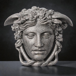 A gray stone textured Medusa head sculpture with snakes for hair and under the chin, against a dark background.