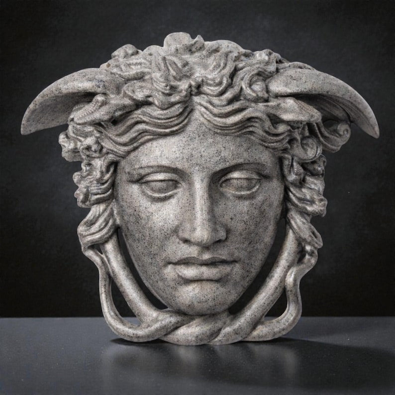 A gray stone textured Medusa head sculpture with snakes for hair and under the chin, against a dark background.