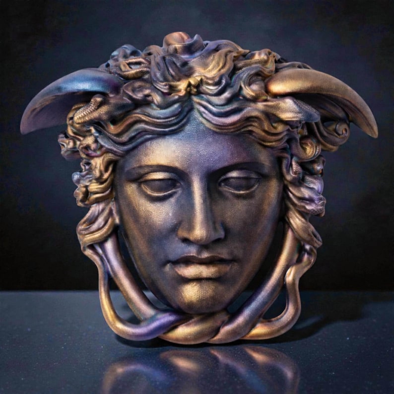 An iridescent Medusa head sculpture with snakes for hair and under the chin, showing purple, blue, and gold hues against a dark background.