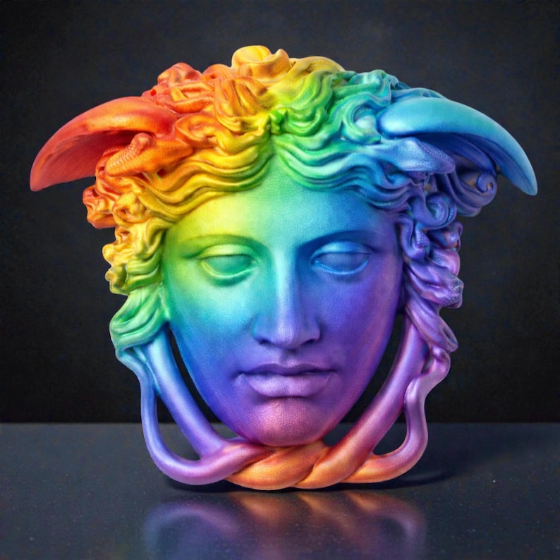 A rainbow-colored Medusa head sculpture with snakes for hair and under the chin, against a dark background.