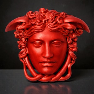 A bright red Medusa head sculpture with serpent hair and a braided chin piece, set against a dark background.