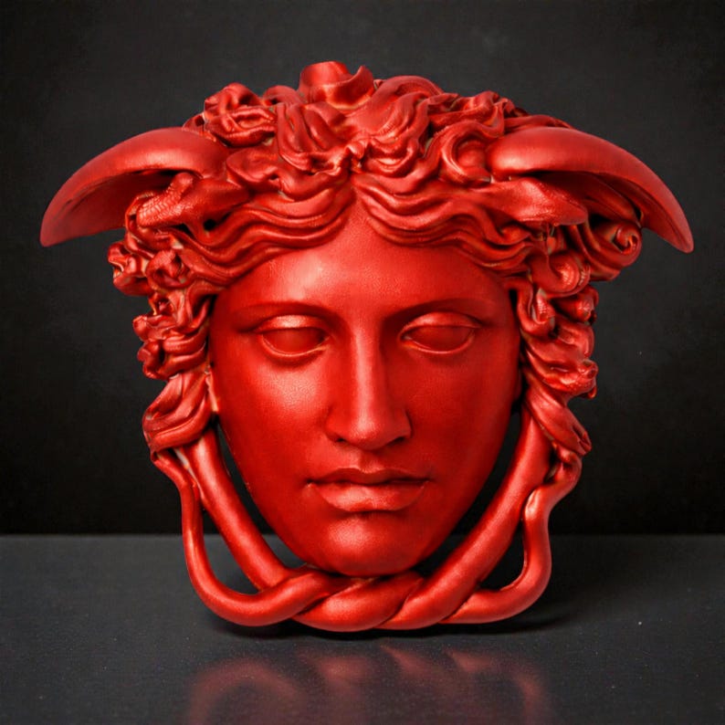 A bright red Medusa head sculpture with serpent hair and a braided chin piece, set against a dark background.