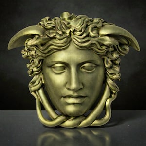 A gold-colored Medusa head sculpture with serpent hair and a braided chin piece, set against a dark background.