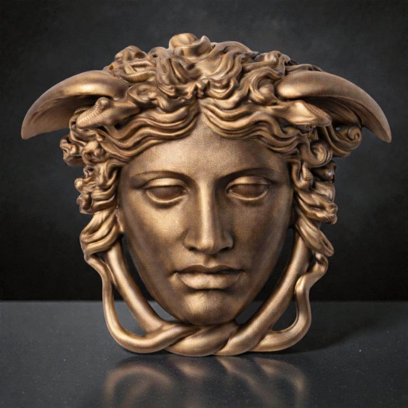 A light bronze Medusa head sculpture with snakes for hair and under the chin, against a dark background.