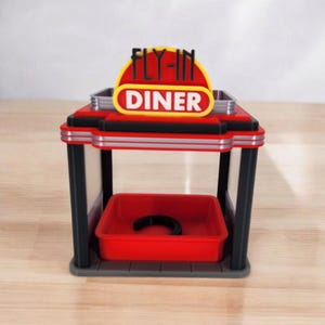 A red, black, and gray retro diner-style bird feeder with "FLY-IN DINER" on its sign is shown from the front on a white surface.
