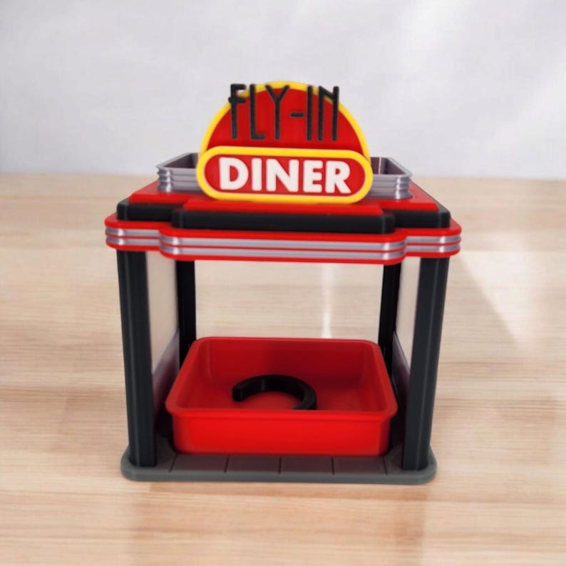 A red, black, and gray retro diner-style bird feeder with "FLY-IN DINER" on its sign is shown from the front on a white surface.