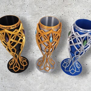 Three 3D-printed goblets in gold, silver, and blue, each with a black or silver interior and elven script, are displayed on a gray textured surface.