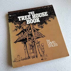 May include: A spiral-bound book titled The Tree House Book by David Stiles with a tan cover featuring a black ink illustration of a treehouse, children climbing a ladder, a dog, and a bucket on a rope, with the title text in bold white letters.