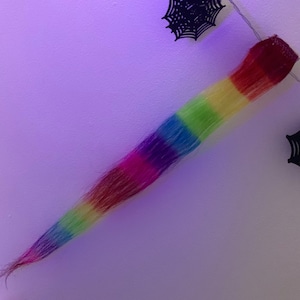 Op de afbeelding: Een lange, regenboogkleurige haarverlenging met een donkerbruine clip aan de bovenkant.