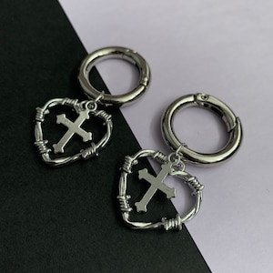 Puede incluir: Dos llaveros plateados con un diseño de corazón de alambre de púas y un dije de cruz plateada.