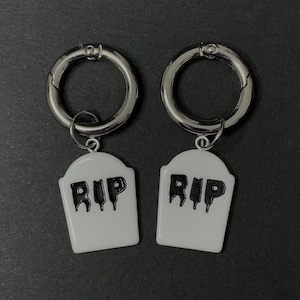 May include: Two silver hoop earrings with white tombstone charms that say "RIP" in black lettering.
