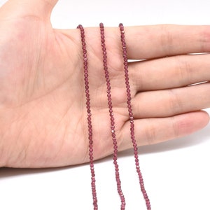 Puede incluir: Tres hebras de cuentas de piedras preciosas de color rojo oscuro, probablemente granates, enhebradas en un alambre fino. Las cuentas son pequeñas y uniformes en tamaño, creando un aspecto delicado y elegante.