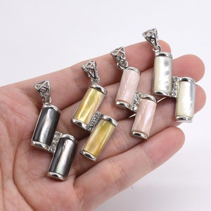 Può includere: Tre ciondoli d'argento con un design geometrico. Ogni ciondolo presenta due pezzi rettangolari di conchiglia, uno bianco, uno rosa e uno giallo. I ciondoli sono collegati da una catena d'argento.