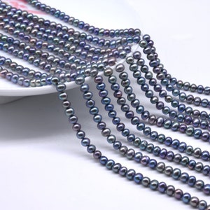 May include: Strands of dark gray pearls with iridescent sheen. The pearls are small and round, strung together to create multiple necklaces. The pearls are displayed on a white surface, suggesting jewelry or craft supplies.