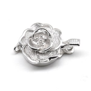 Puede incluir: Cierre de flor de rosa plateado para la elaboración de joyas. El cierre está detallado con una superficie texturizada y un pequeño bucle para sujetarlo a un collar o pulsera.