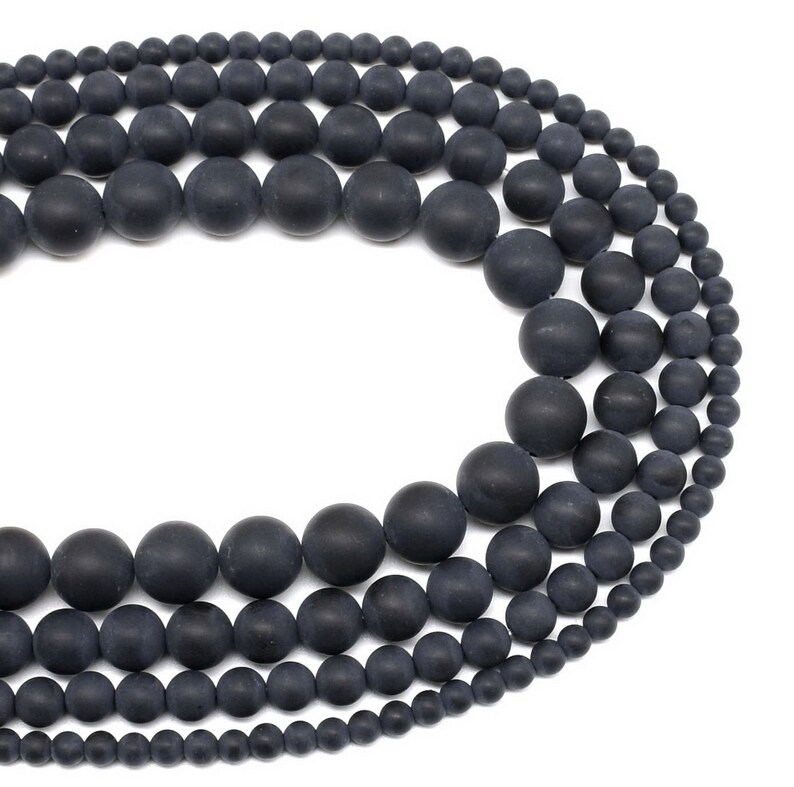 May include: A strand of black matte round beads of varying sizes. The beads are strung together on a clear thread.