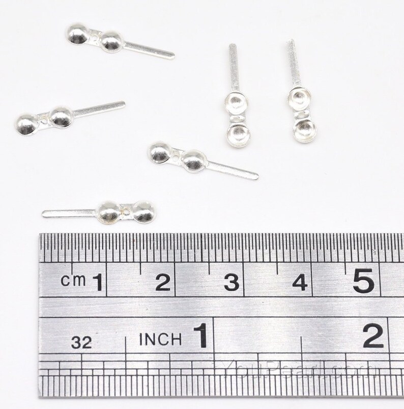 May include: Five silver-toned metal bead caps with a straight pin. The bead caps are approximately 1 inch long and have two round beads. The bead caps are shown on a ruler with inch and centimeter markings.