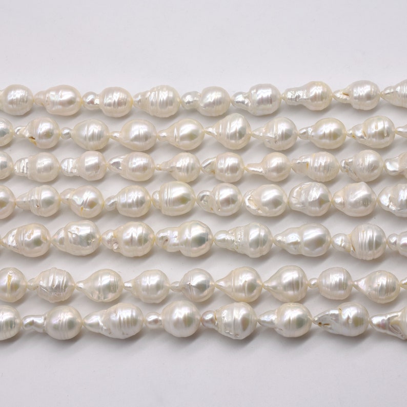 May include: A strand of white baroque pearls, with a slightly irregular shape, arranged in rows on a white background.