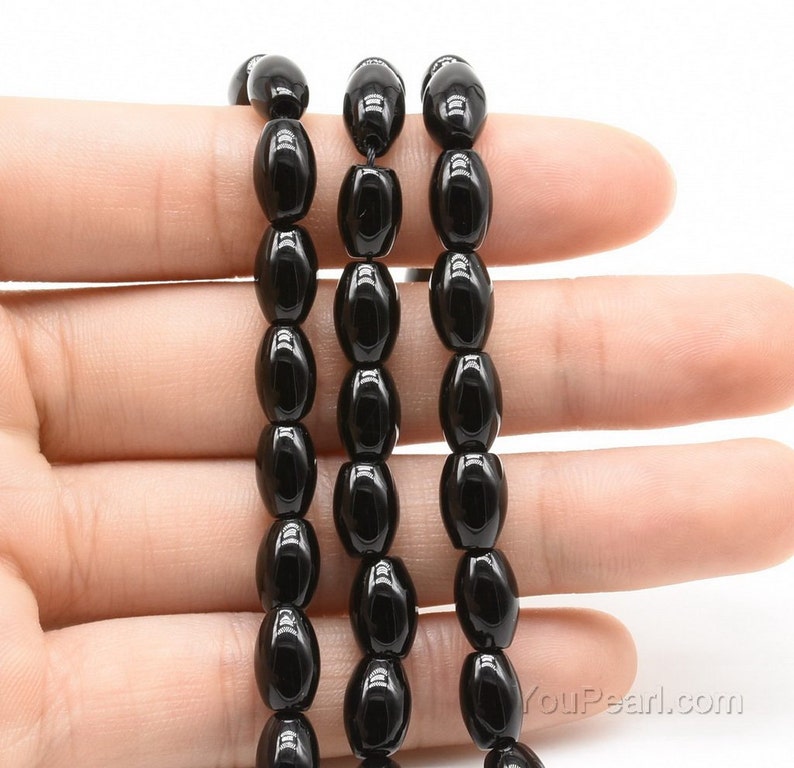 May include: A strand of black oval-shaped gemstone beads. The beads are smooth and polished, and they have a glossy finish.