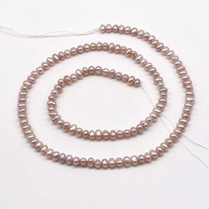 May include: A strand of pale pink freshwater pearls, strung on white thread. The pearls are small and irregular in shape, with a slightly iridescent sheen.