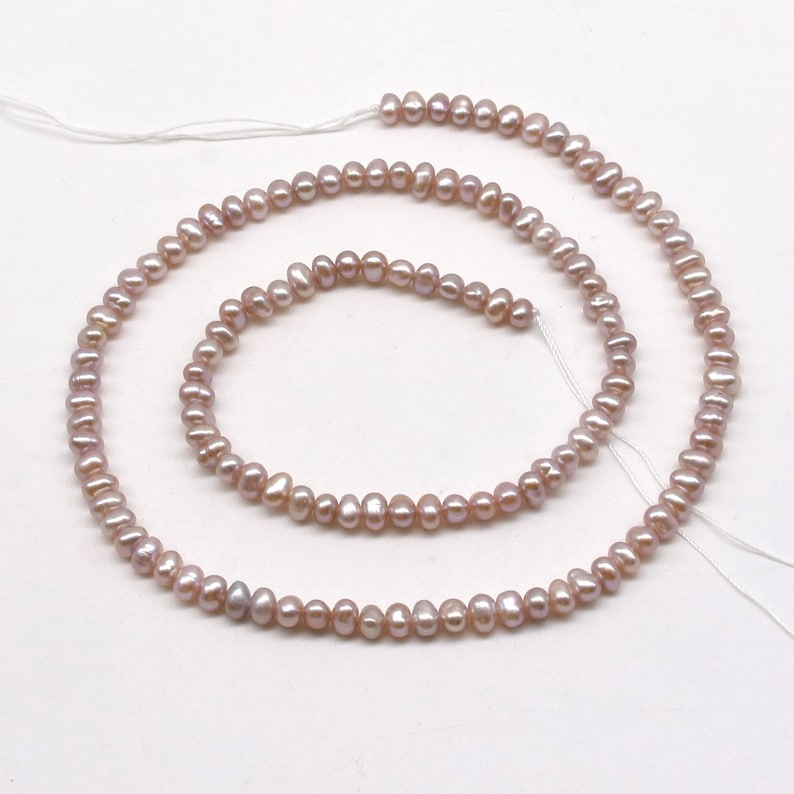 May include: A strand of pale pink freshwater pearls, strung on white thread. The pearls are small and irregular in shape, with a slightly iridescent sheen.