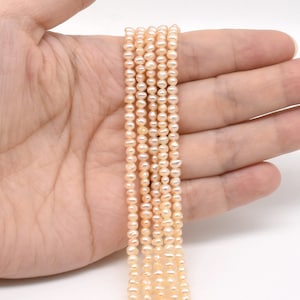 Könnte beinhalten: Eine Strähne kleiner, blassrosa Süßwasserperlen. Die Perlen sind rund und glatt und auf einem dünnen Faden aufgefädelt. Die Perlen haben einen Durchmesser von etwa 4 mm.