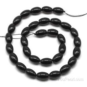 May include: A strand of black oval-shaped gemstone beads. The beads are strung on a black thread and are approximately 10mm in length.