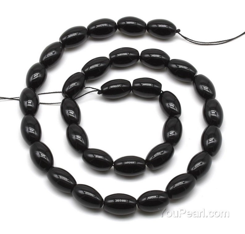 May include: A strand of black oval-shaped gemstone beads. The beads are strung on a black thread and are approximately 10mm in length.