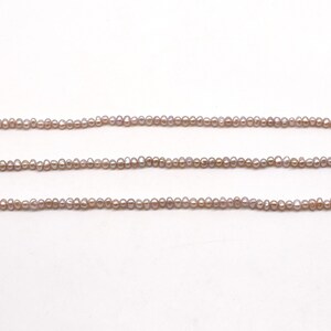 May include: A strand of small, pale lavender freshwater pearls. The pearls are strung on a clear thread and are arranged in a straight line.