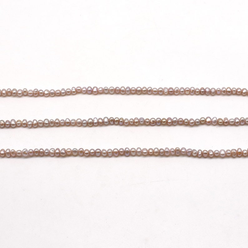 May include: A strand of small, pale lavender freshwater pearls. The pearls are strung on a clear thread and are arranged in a straight line.