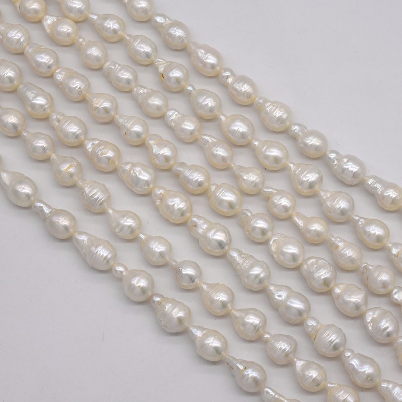 May include: A strand of white freshwater pearls with a baroque shape. The pearls are strung on a white thread and are arranged in a staggered pattern.