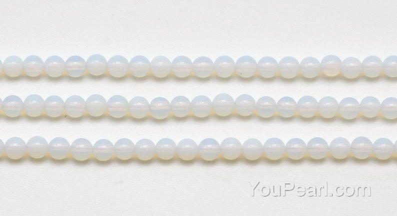 May include: A strand of white opaque round glass beads. The beads are strung on a clear thread and are arranged in three rows.