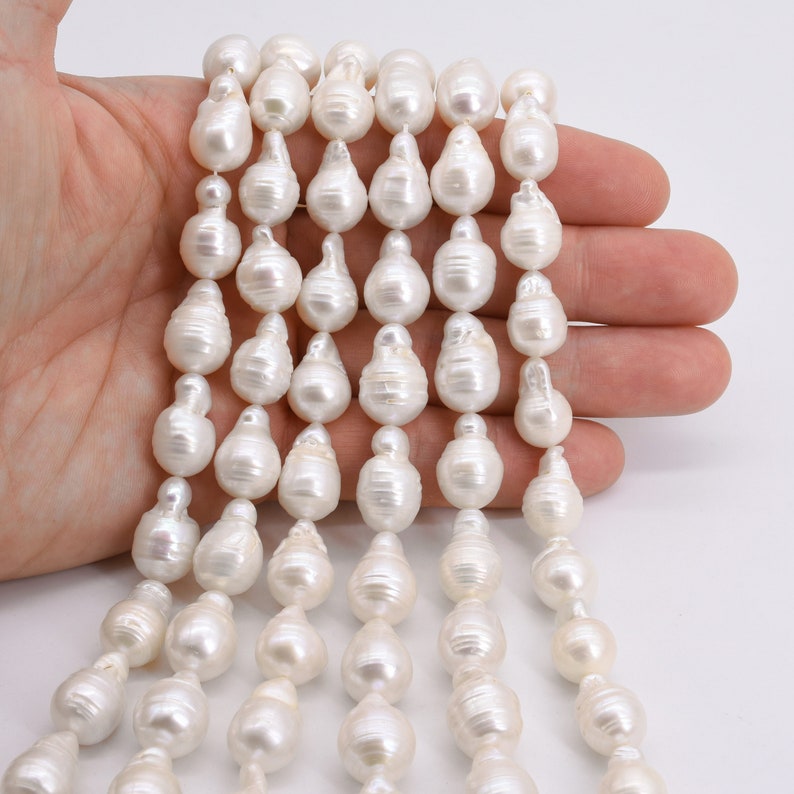 May include: A strand of white baroque pearls, each pearl is a unique, irregular shape. The pearls are strung on a white thread and are approximately 10mm in size.