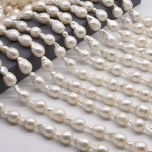 May include: A strand of white baroque pearls, each pearl is a unique shape and size. The pearls are strung on a white thread and are arranged in a staggered pattern.