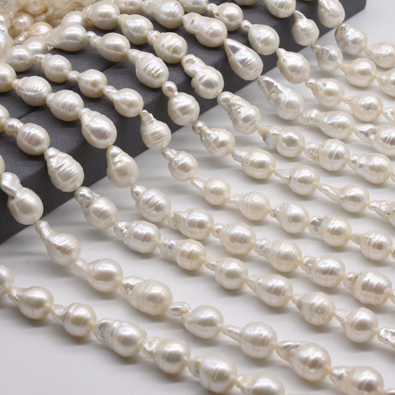 May include: A strand of white baroque pearls, each pearl is a unique shape and size. The pearls are strung on a white thread and are arranged in a staggered pattern.