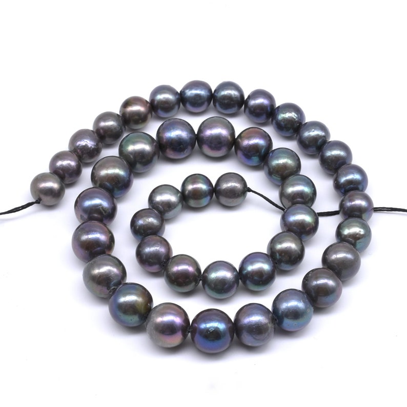 May include: A strand of black pearls with iridescent hues. The pearls are round and smooth, and they are strung on a black thread.