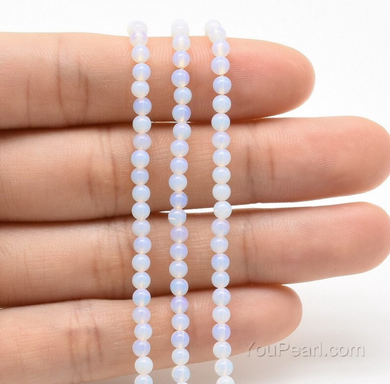May include: Three strands of white opal beads, each strand is approximately 16 inches long. The beads are round and have a smooth, polished finish. The beads are strung on a clear elastic cord.