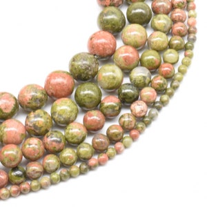 May include: Strands of unakite gemstone beads in varying sizes. The beads display a mix of olive green and salmon pink colors. The beads are round and polished, with a natural, speckled appearance. The beads are strung together, ready for jewelry making.