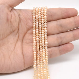May include: A strand of pale pink freshwater pearls, strung on a thin thread. The pearls are small and round, with a smooth, glossy finish.