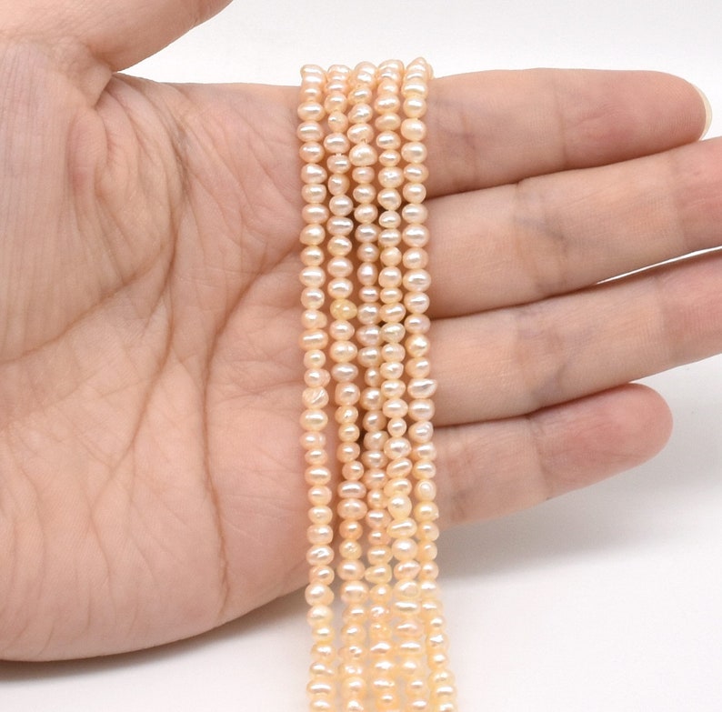 May include: A strand of pale pink freshwater pearls, strung on a thin thread. The pearls are small and round, with a smooth, glossy finish.