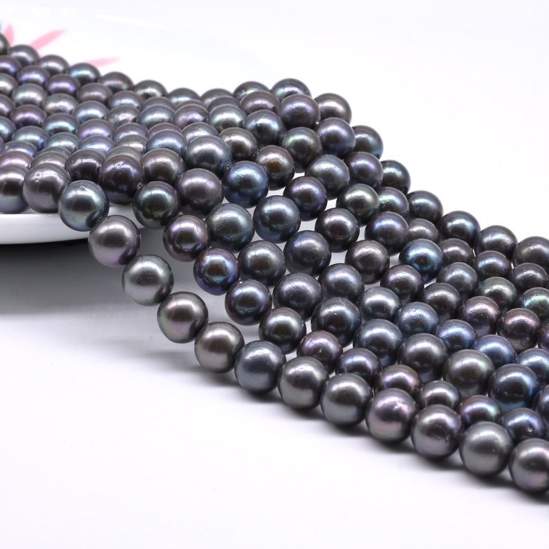 May include: A strand of black freshwater pearls. The pearls are round and have a slight iridescent sheen.