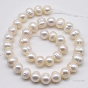 May include: A strand of white freshwater pearls, with a smooth, round shape. The pearls are strung on a white thread and are arranged in a circular pattern.