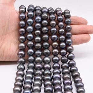 May include: A strand of black freshwater pearls with a slight iridescent sheen. The pearls are round and smooth, and they are strung on a clear thread.