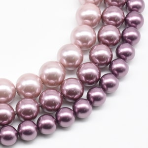 Puede incluir: Una hebra de perlas falsas en tonos rosa, morado y lavanda. Las perlas están dispuestas en un patrón degradado, con el tono más claro en la parte superior y el tono más oscuro en la parte inferior.