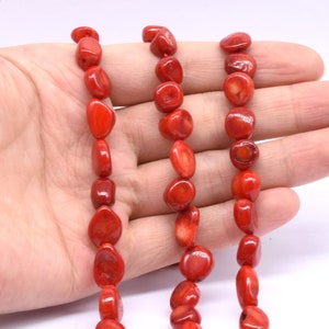 Puede incluir: Tres hebras de cuentas de coral rojo, cada hebra está hecha de cuentas lisas de forma ovalada. Las cuentas son de un color rojo vibrante y tienen un aspecto natural y orgánico.
