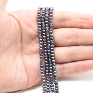 May include: A strand of black freshwater pearls with iridescent blue and green hues. The pearls are small and round, and they are strung on a thin thread.