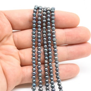 May include: A strand of dark gray freshwater pearls, approximately 6mm in diameter. The pearls are strung on a clear thread and are ready for jewelry making.