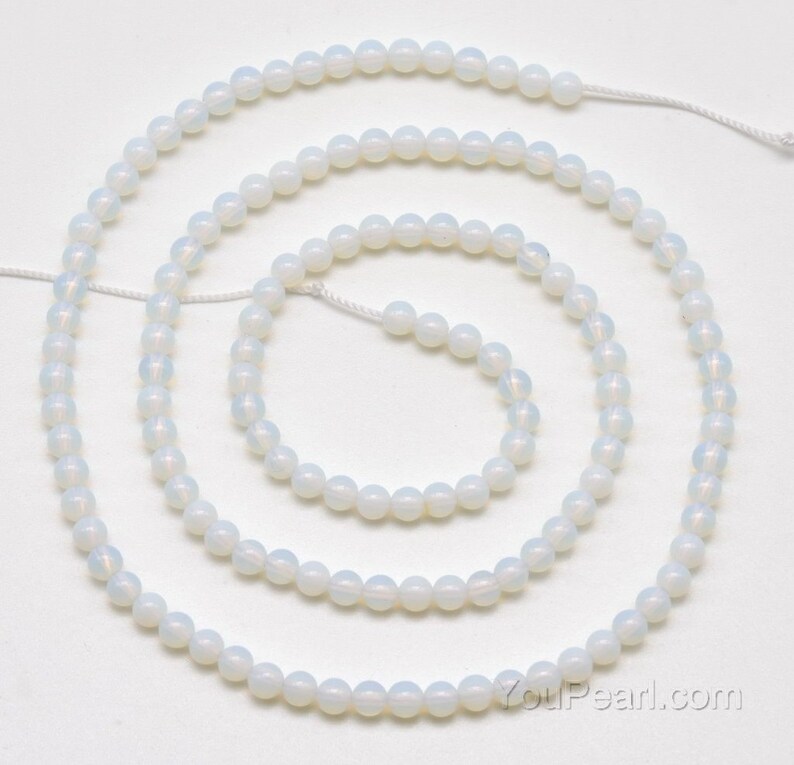 May include: A strand of white opal beads, approximately 6mm in diameter, strung on a white thread. The beads are round and have a smooth, polished finish.