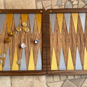 May include: A wooden backgammon set with a walnut finish. The board is open and shows the playing surface with silver and gold triangles. There are checkers on the board and dice in the tray.