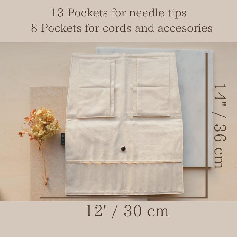 May include: A cream-colored fabric organizer case featuring 13 pockets for needle tips and 8 pockets for cords and accessories. The case measures 14 inches in height and 12 inches in width, with a central snap closure and a small side label.